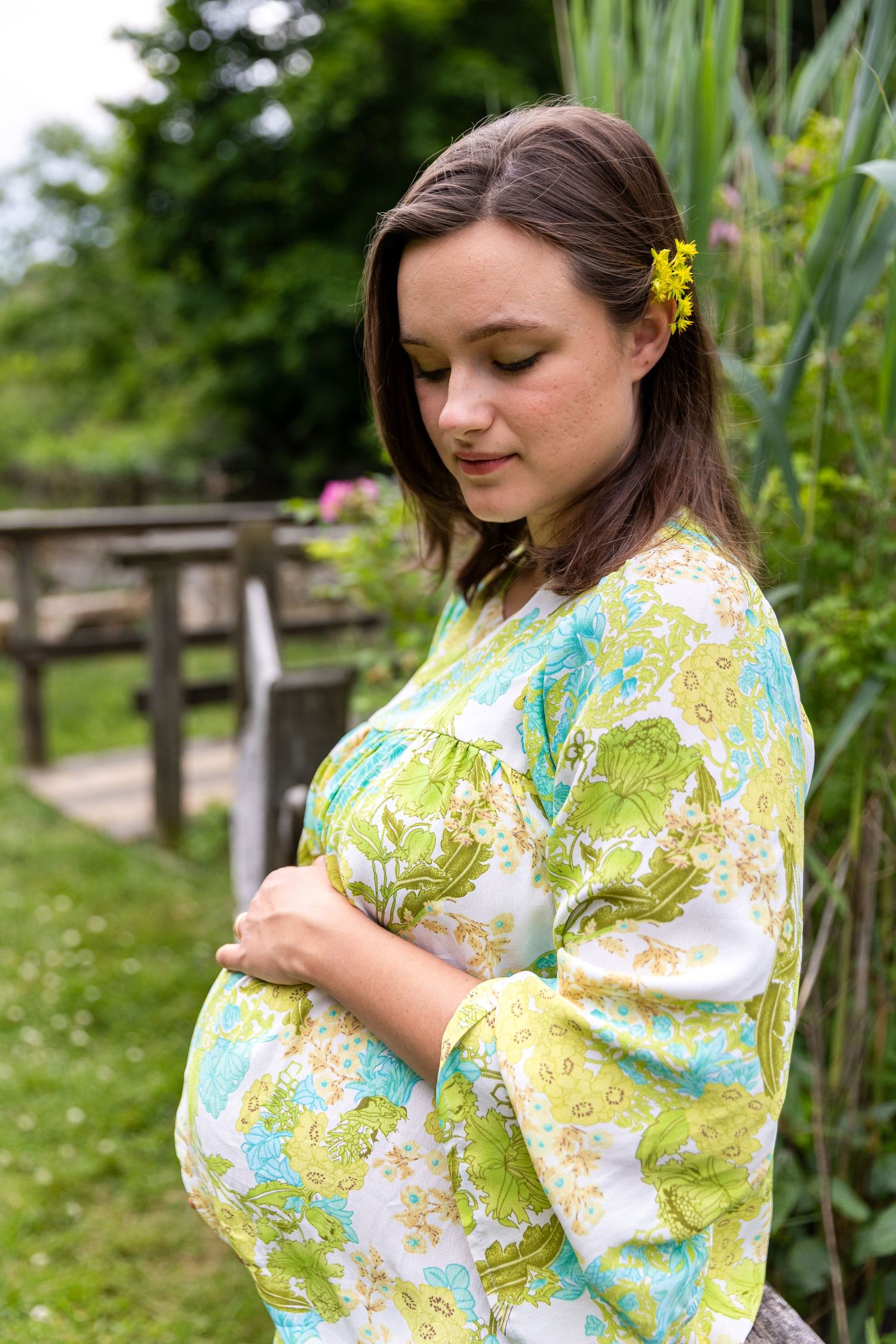 Person wearing a vibrant floral kimono-style robe stands in a lush garden setting with blooming flowers and greenery.