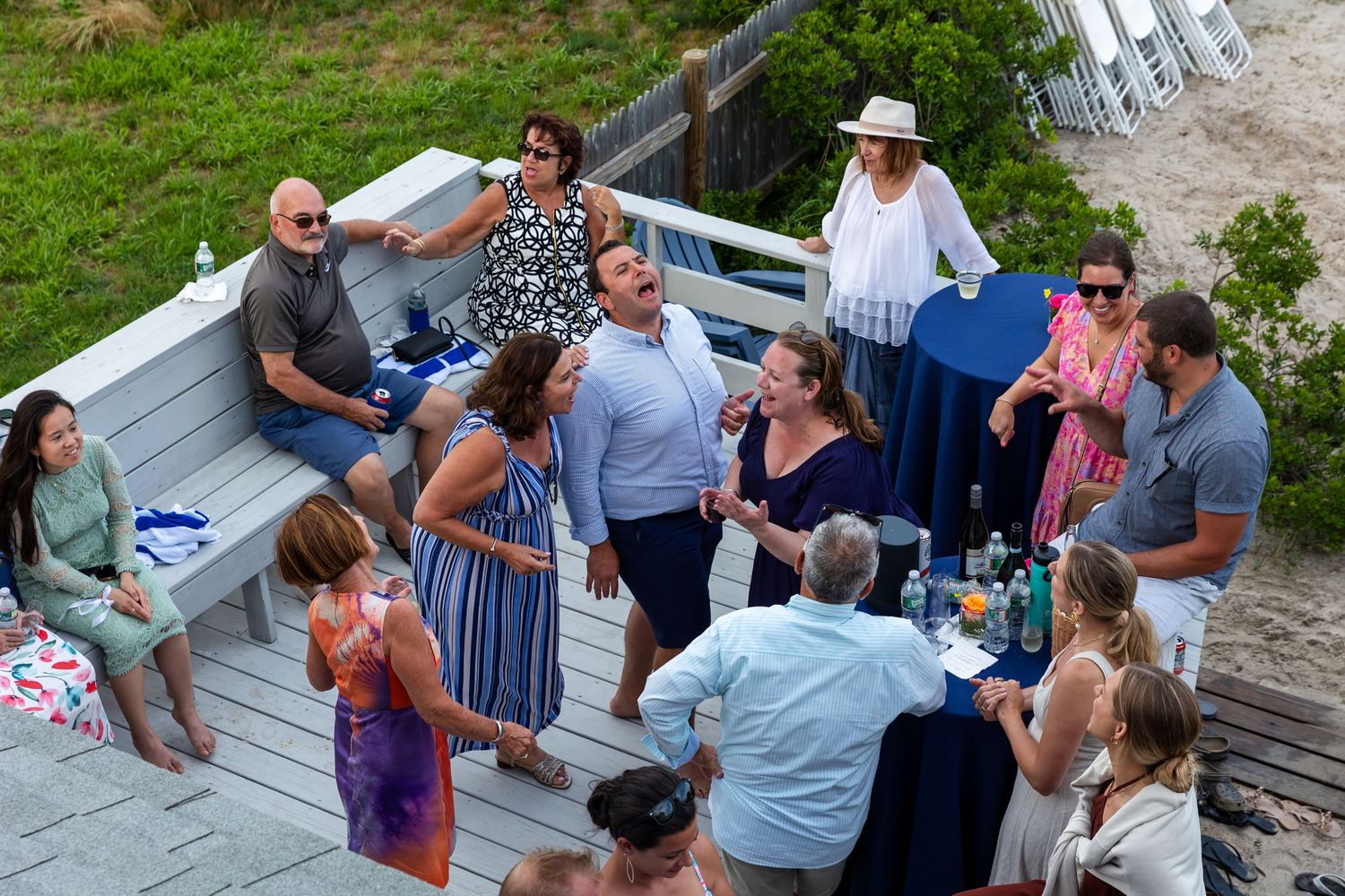 A group of people gather for a social event on an outdoor wooden deck during daytime.