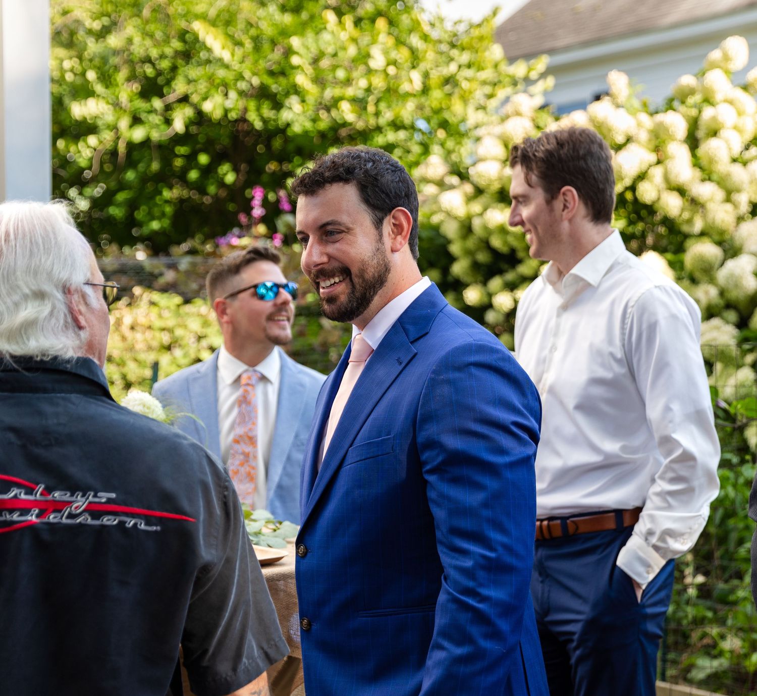 A group of people having a conversation outdoors in a garden setting with blooming flowers and sunlight.