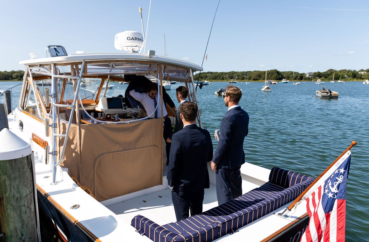 Group standing on a docked boat with an American flag displayed at the stern on a sunny day at the marina.