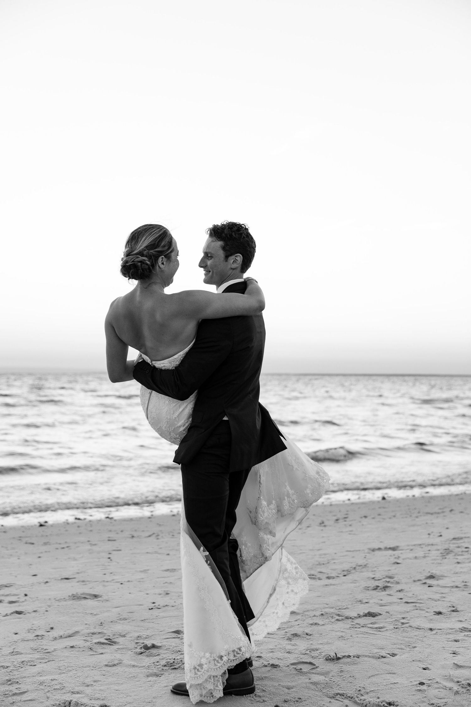 A romantic couple dancing on a scenic beach during sunset in elegant black and white tones.