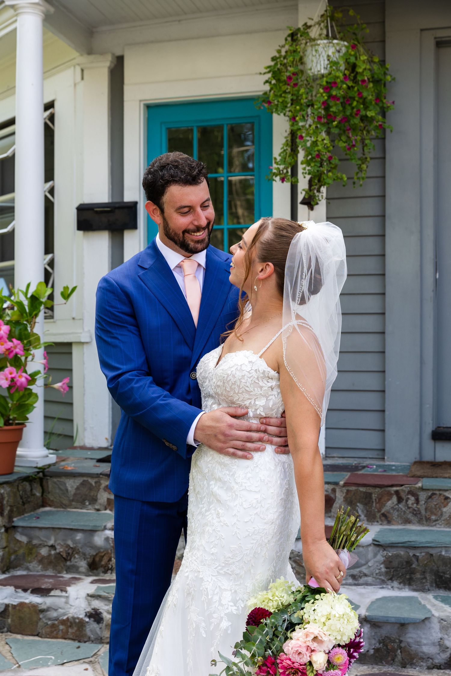 A bride and groom share a candid moment on their wedding day in front of a house with a bright turquoise door.
