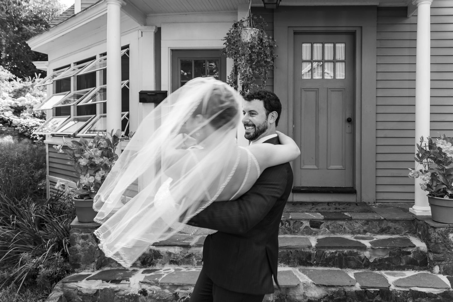 A couple shares a romantic moment while a white veil flows in the wind during their spring outdoor wedding ceremony.
