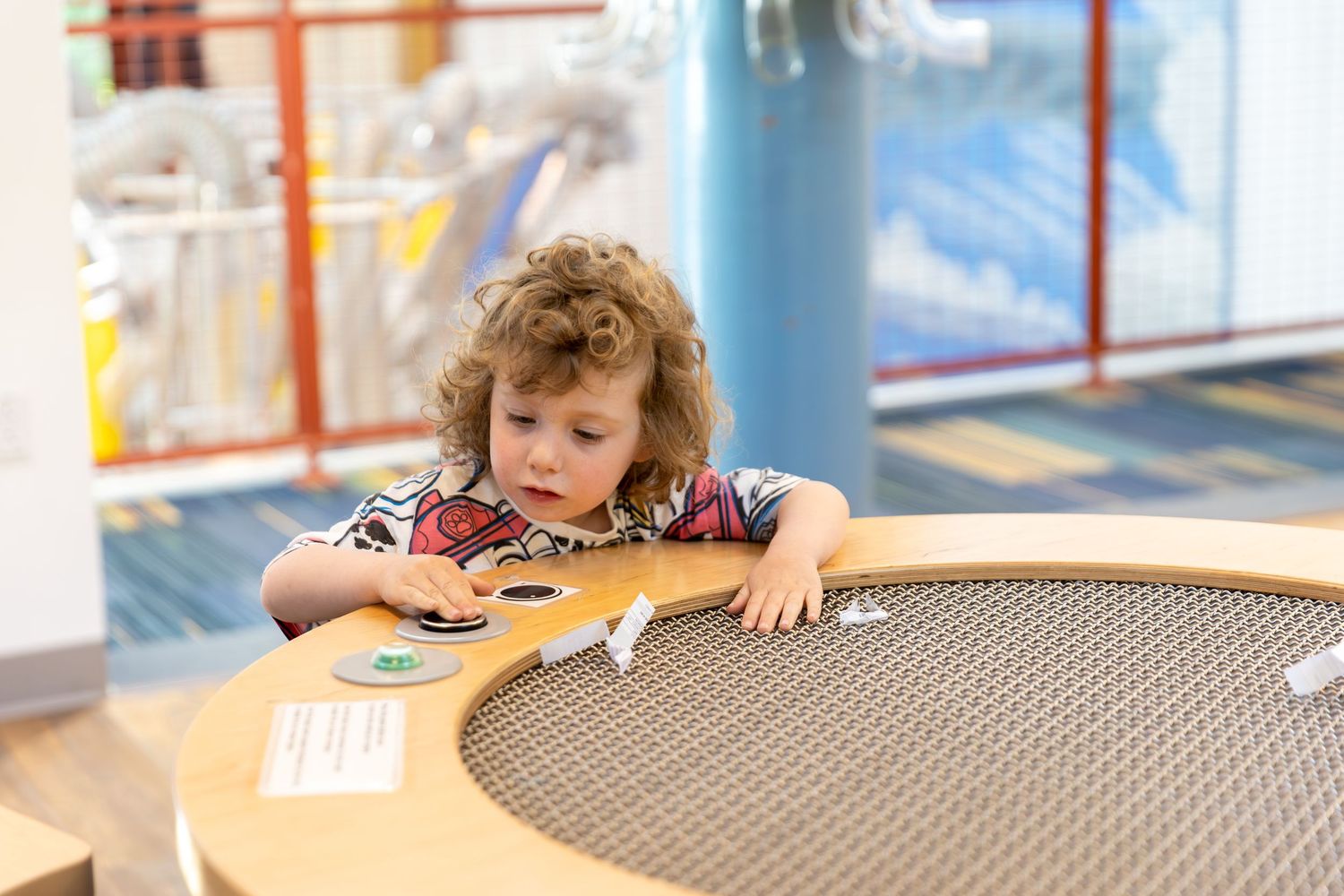 Children sit at round tables in an early learning classroom environment during an educational activity.
