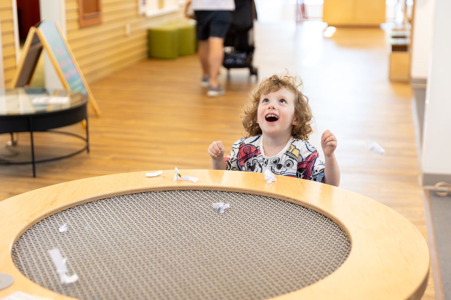 A child jumps excitedly on a round trampoline surface in an indoor play area.