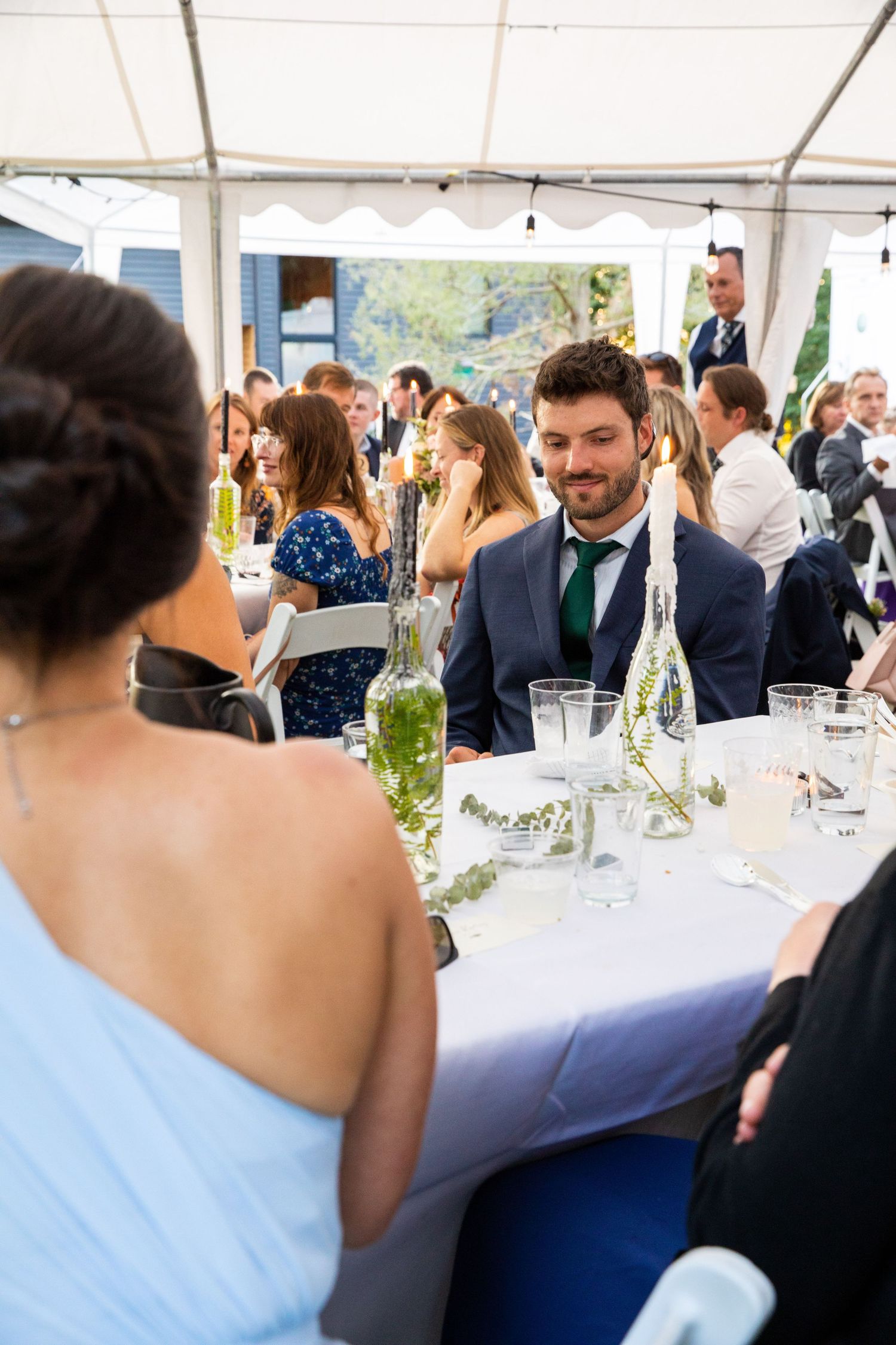 Guests seated at round tables with white tablecloths in an outdoor wedding tent with festive reception atmosphere.
