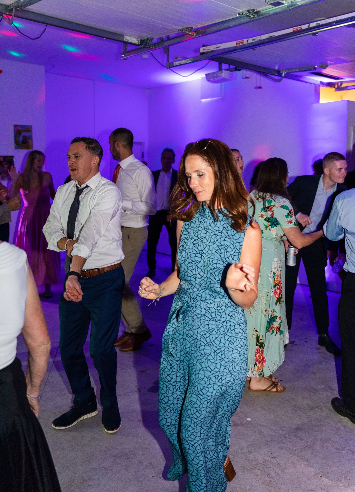People dancing and having fun at a party in a room with purple mood lighting and industrial ceiling.