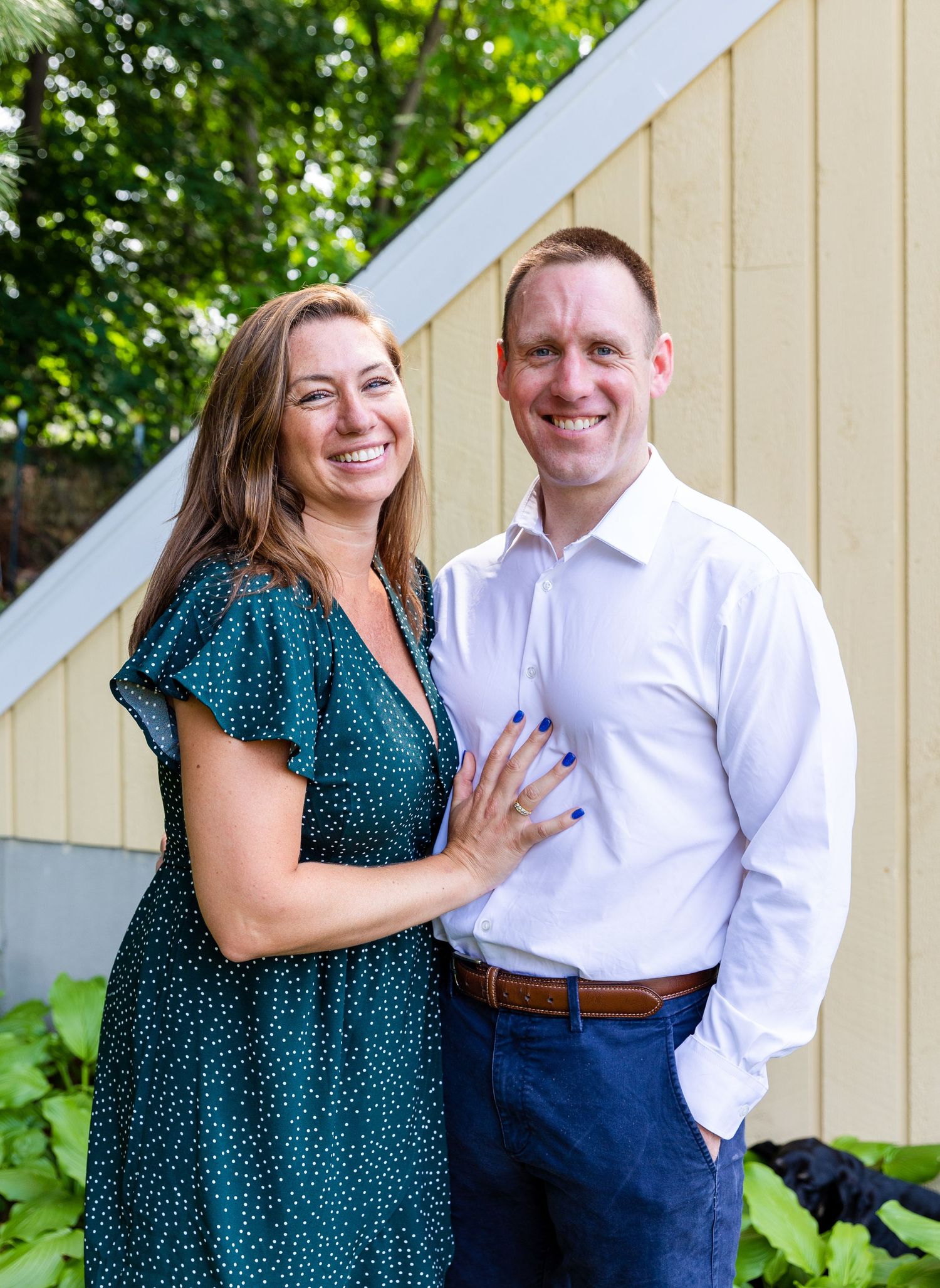 A couple shares intimate moments outdoors, with greenery and a beige wall in the background.