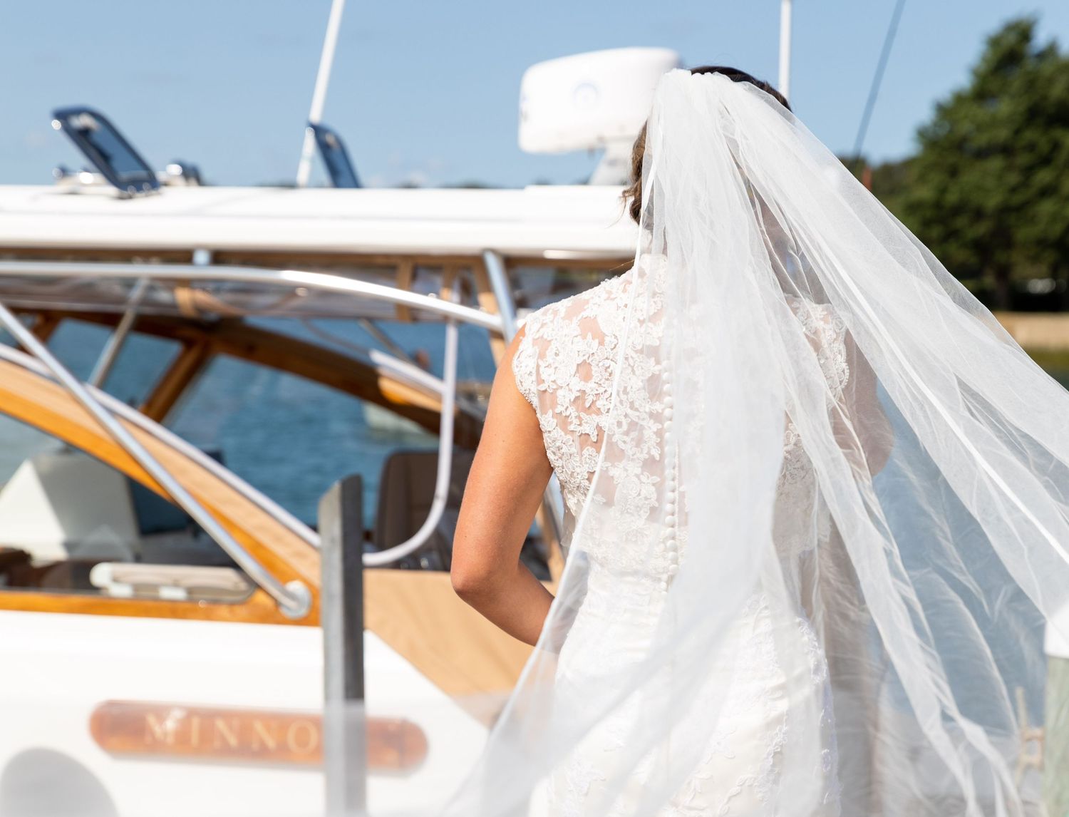 A white wedding gown with lace details and flowing veil visible near a luxury boat deck on a sunny day.