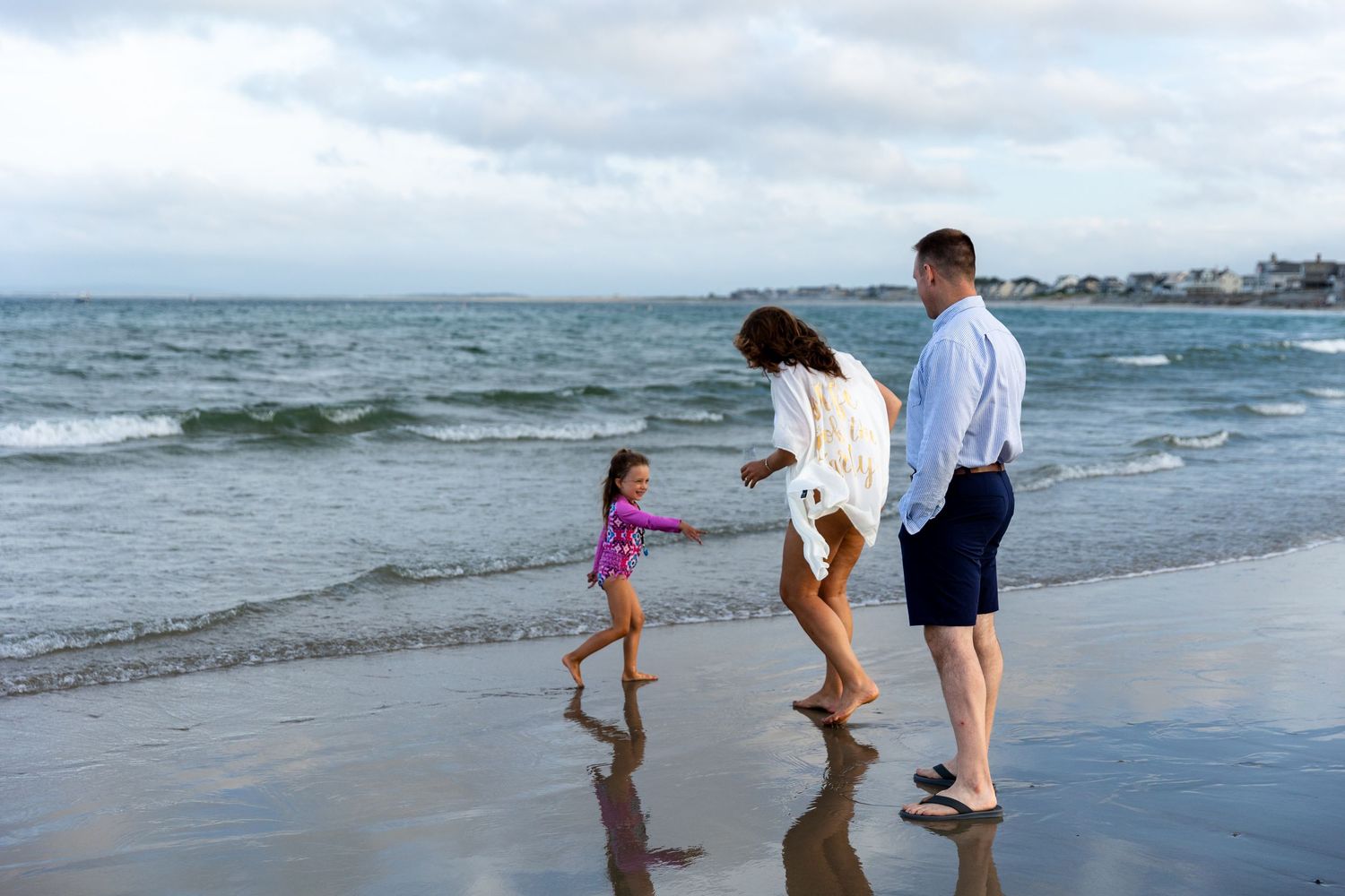 Family walks along sandy beach at sunset as ocean waves roll in during a peaceful evening together.