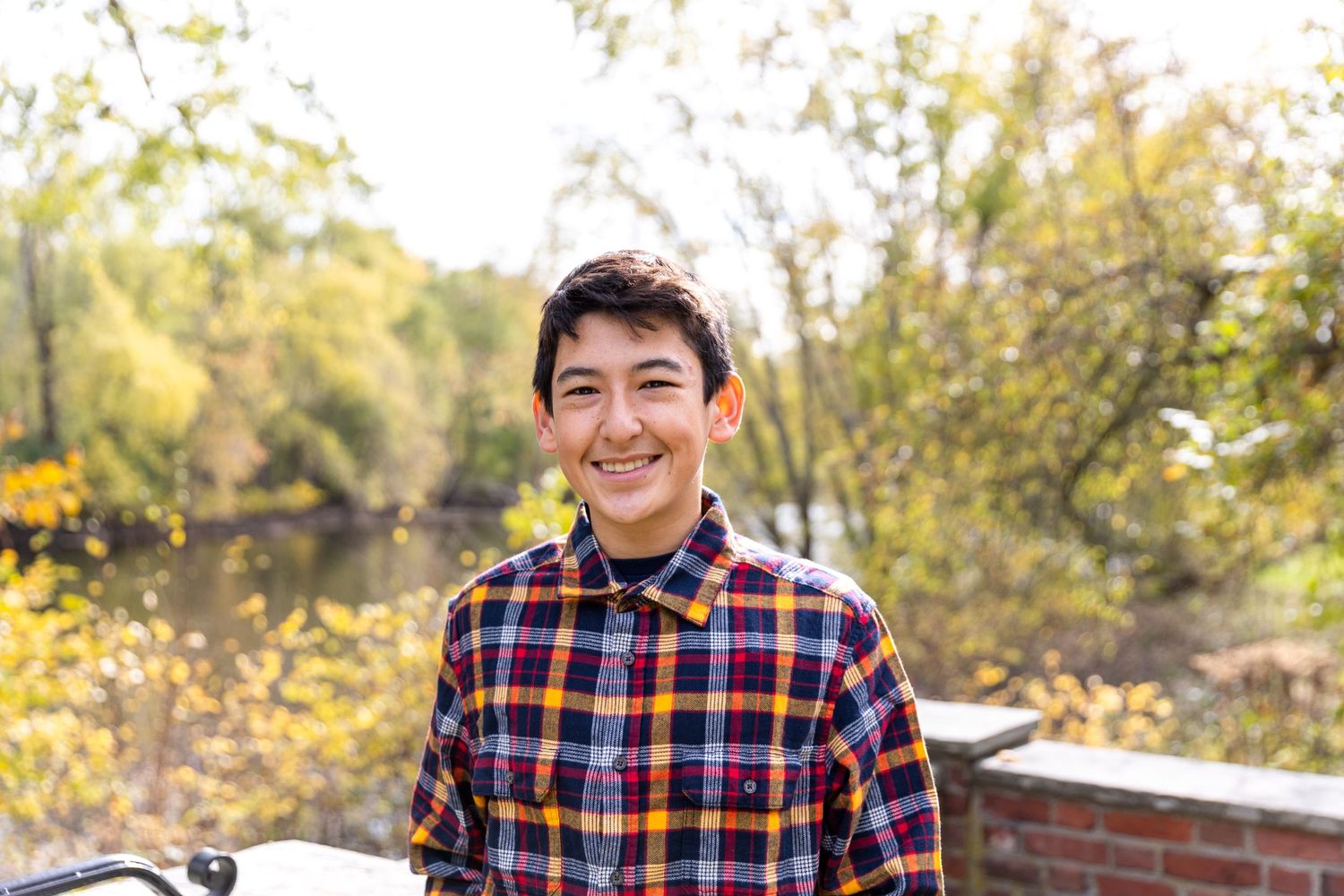 Portrait of person in plaid shirt smiling outdoors during autumn.