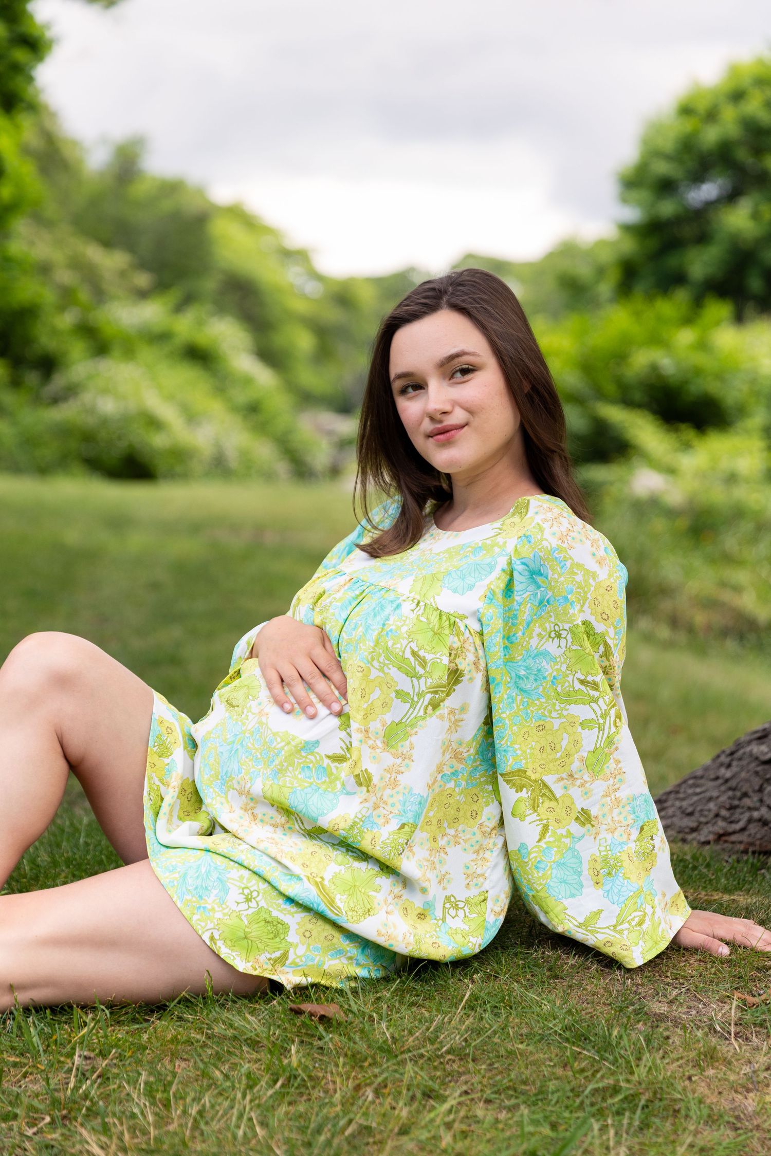 A person wearing a yellow and turquoise floral dress poses laying on grass in a garden setting across multiple shots.