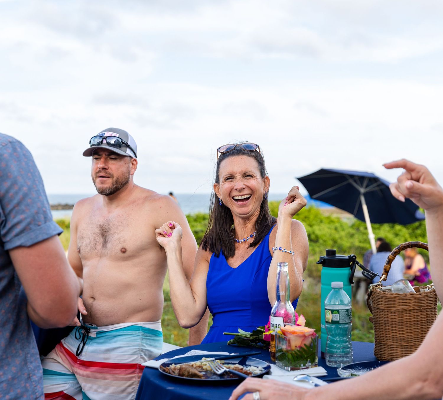 People enjoying an outdoor picnic meal with drinks and snacks on a sunny day.