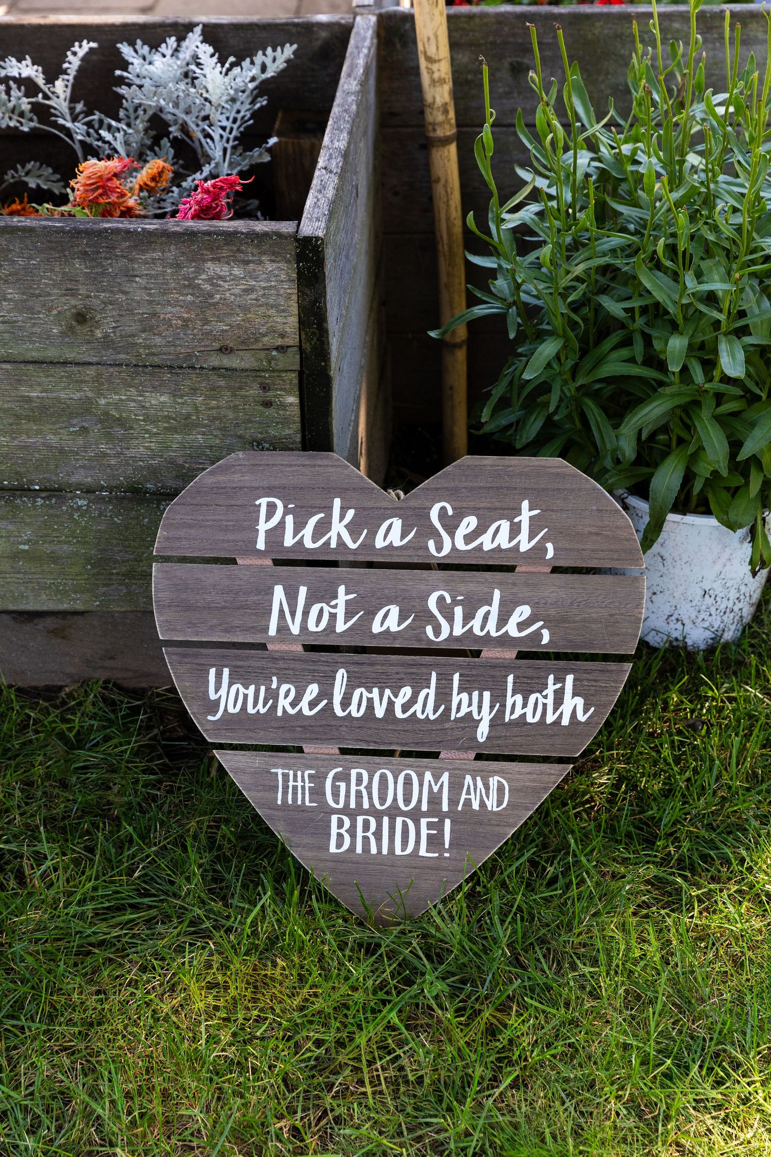 Rustic wooden wedding signs in a garden display messages 'Pick a Seat', 'Not a Side', and encouraging words about love.