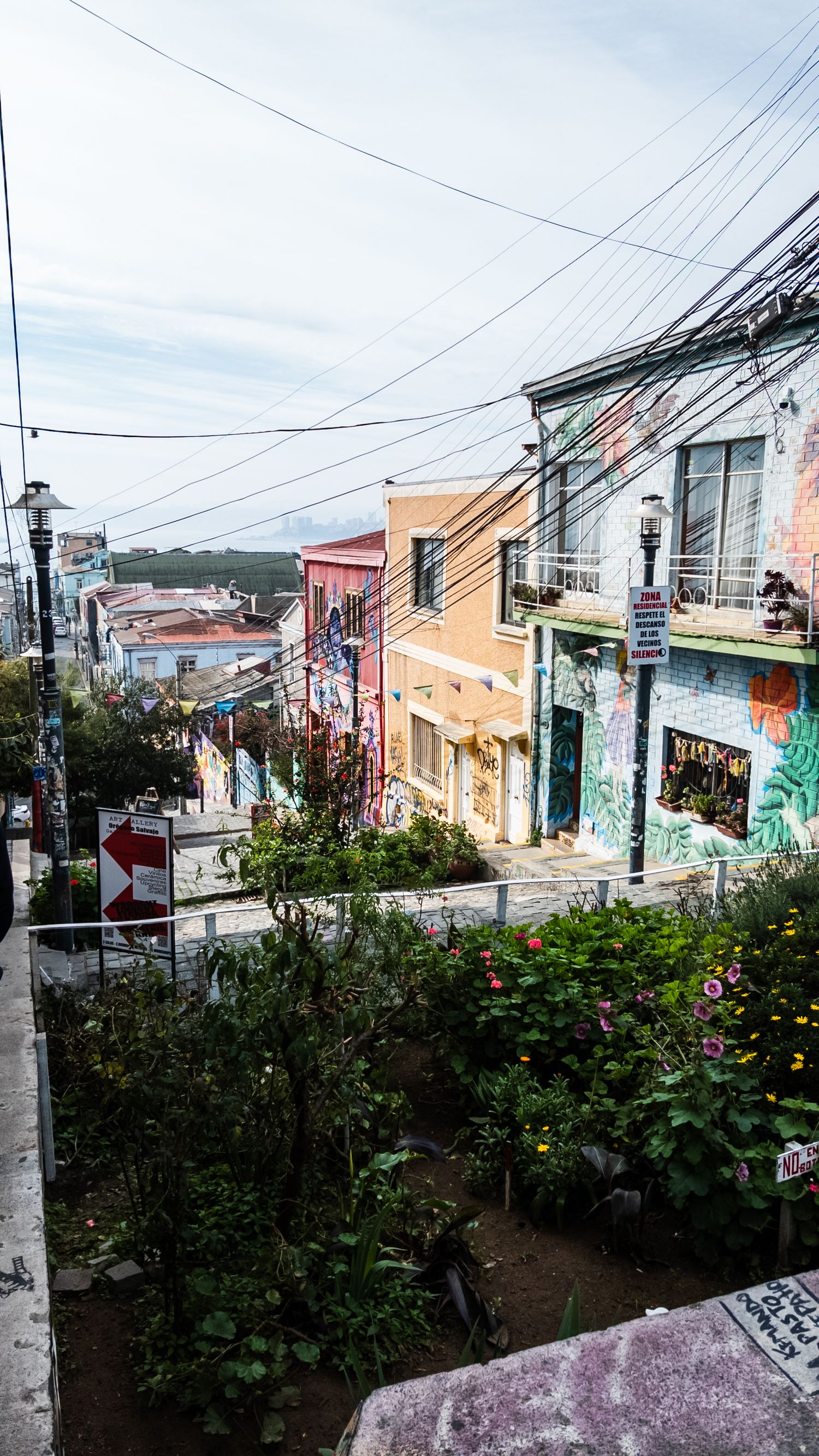 Colorful houses line a steep hillside street with power lines and graffiti in Valparaiso, Chile.