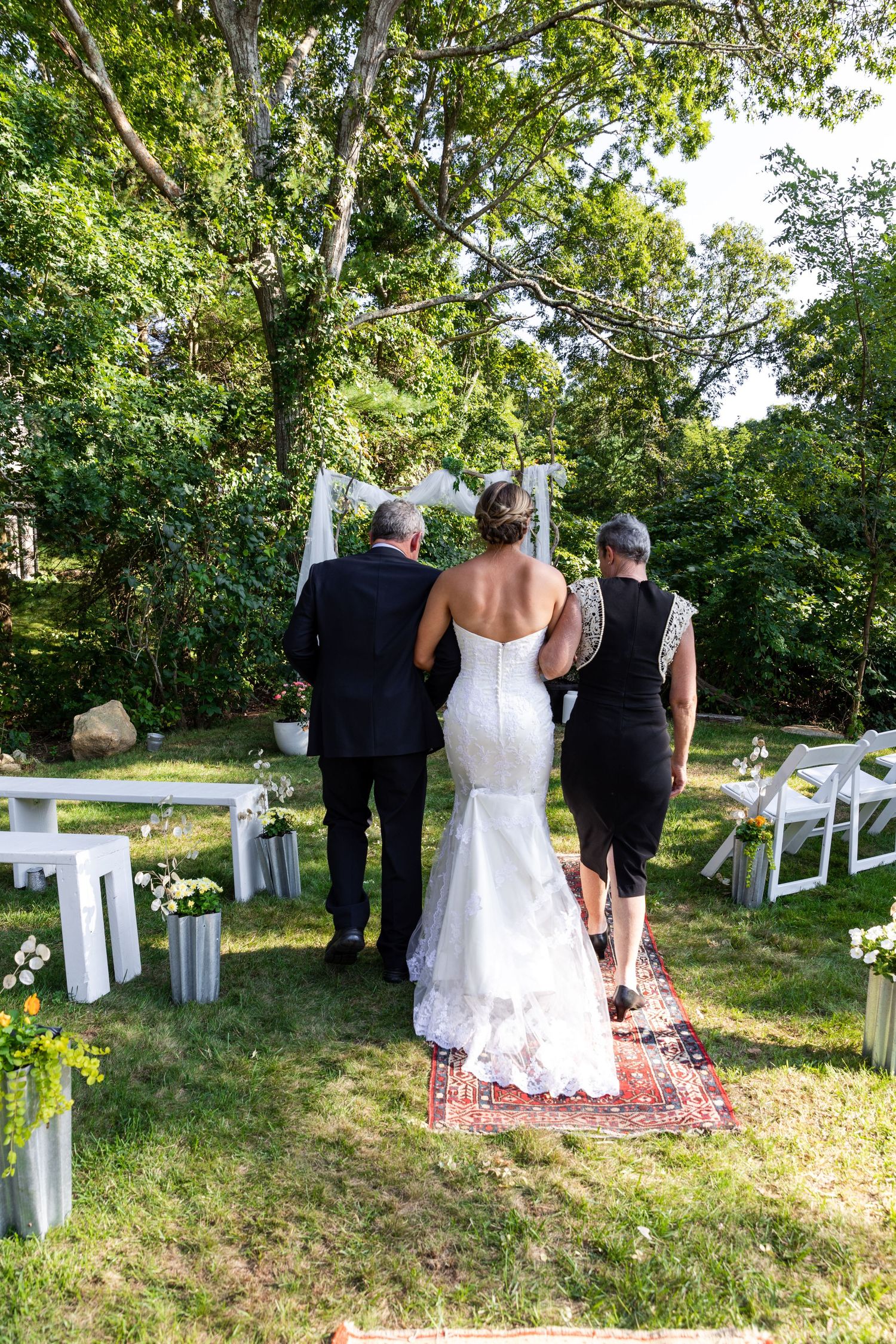 A sunny outdoor garden wedding ceremony setup with chairs and flower petals scattered on grassy lawn path.
