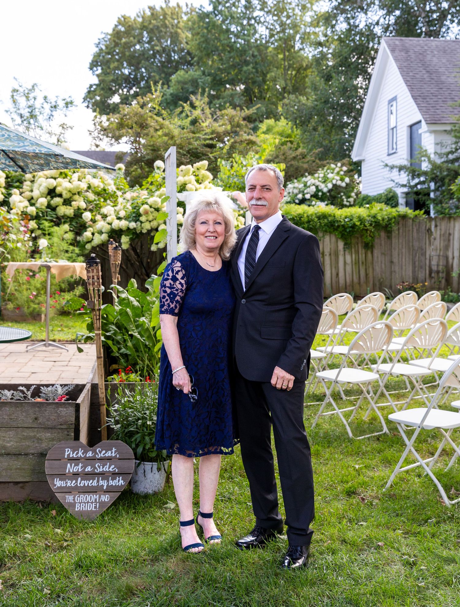 Outdoor wedding venue setup with white folding chairs arranged on a lawn near a wooden privacy fence.