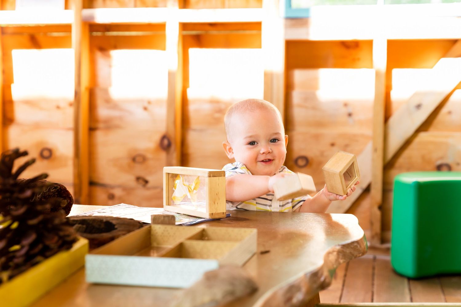 Happy baby sits at wooden table with learning materials in classroom setting.