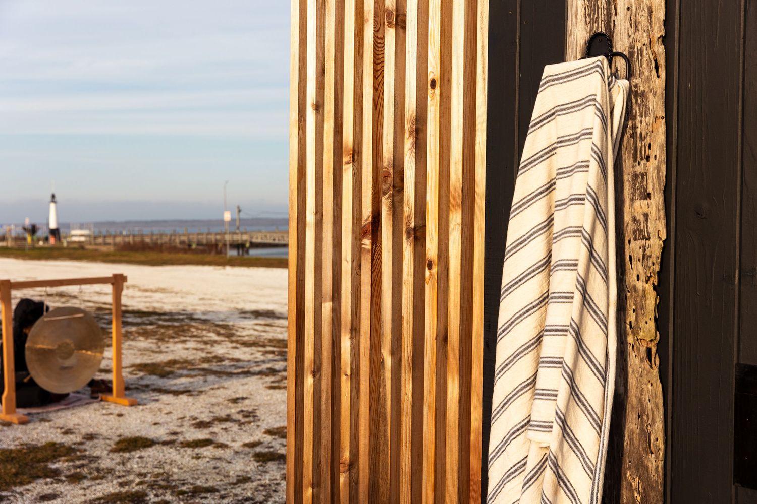 Beach shower area with striped curtain and wooden posts against a sandy beach backdrop on a sunny day.
