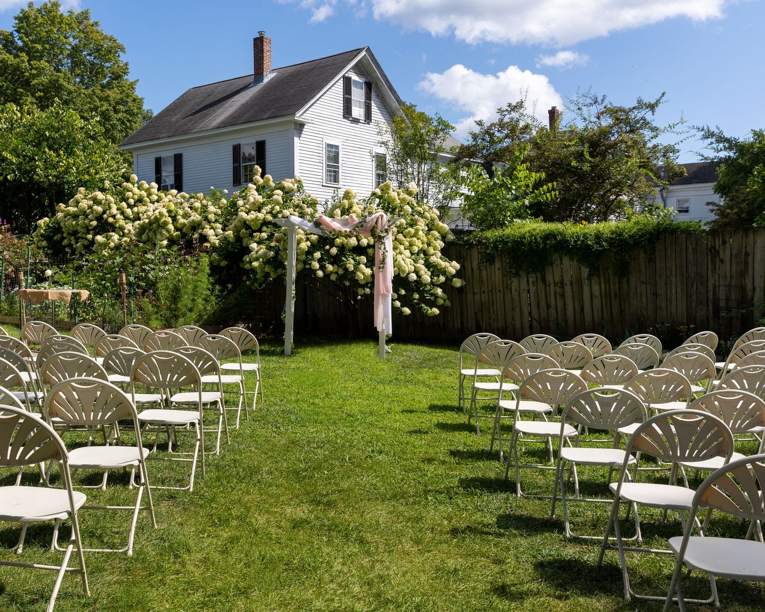 White wooden chairs arranged in rows on a green lawn for an outdoor wedding ceremony setup.