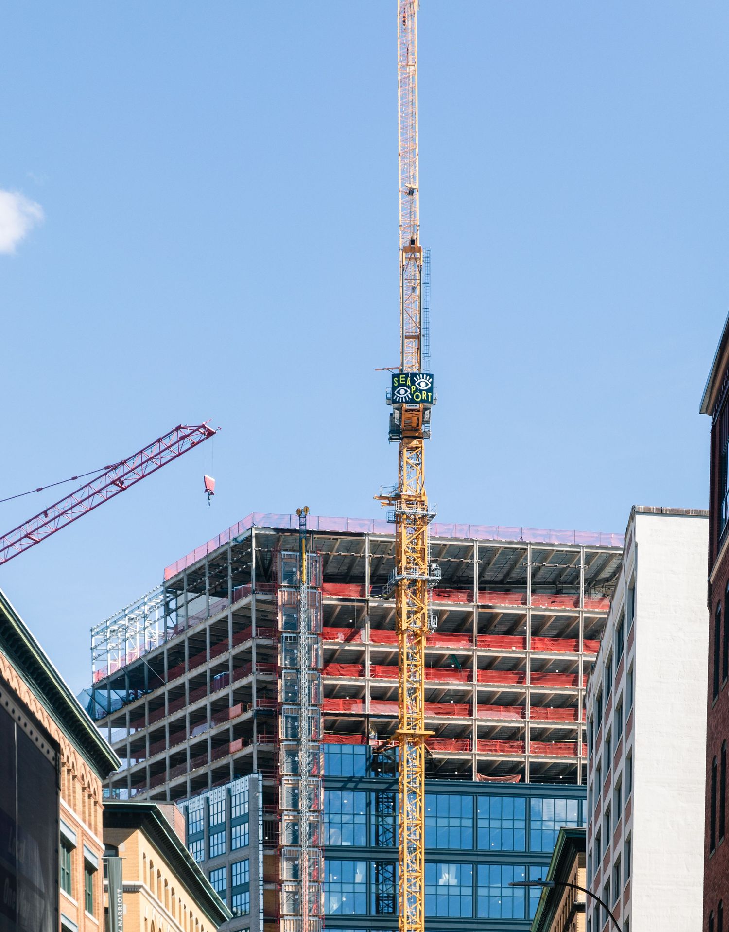 Construction site with tall yellow crane building a modern high-rise structure against blue sky.