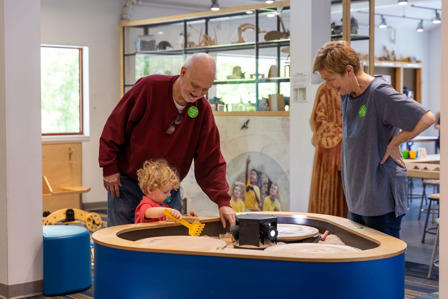 Supportive instructor works with a student on an educational activity at a blue table in a classroom setting.