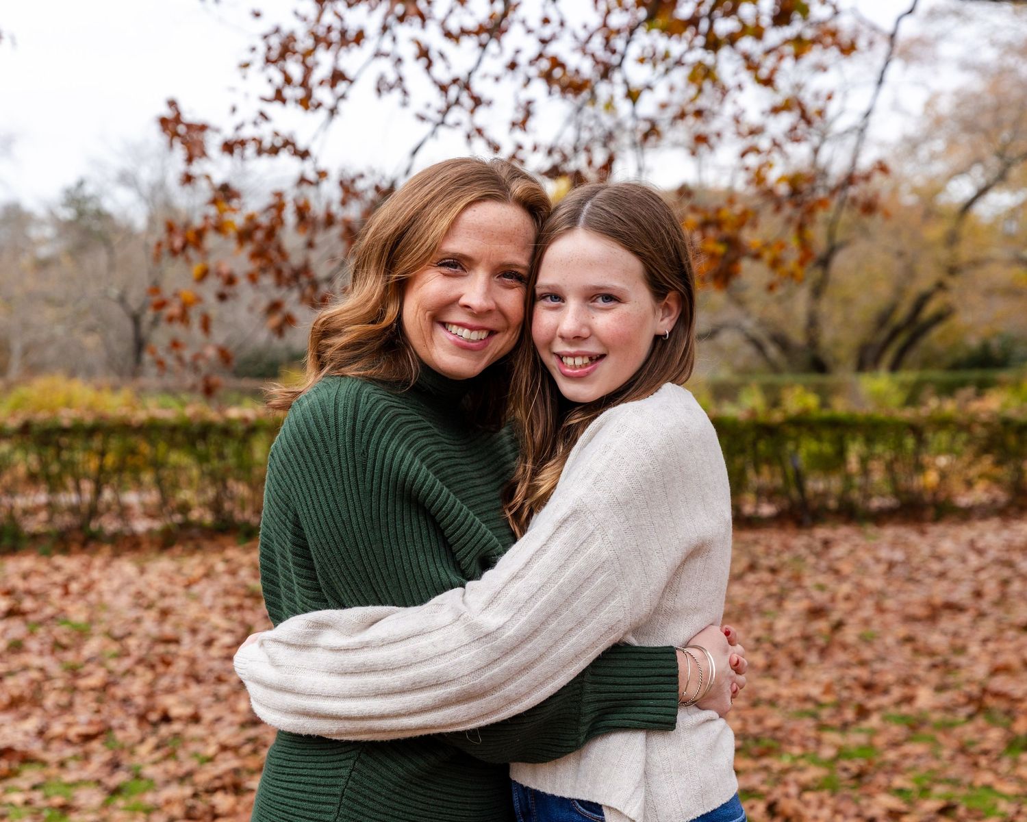 Two people embrace and laugh together while walking through fallen autumn leaves in a park setting.