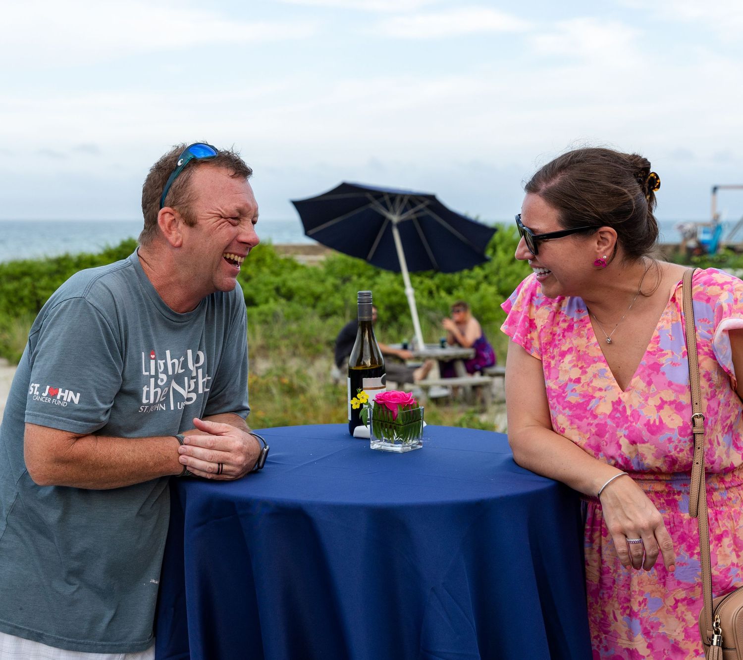 Couple enjoying drinks and conversation at an outdoor table with a navy blue tablecloth.