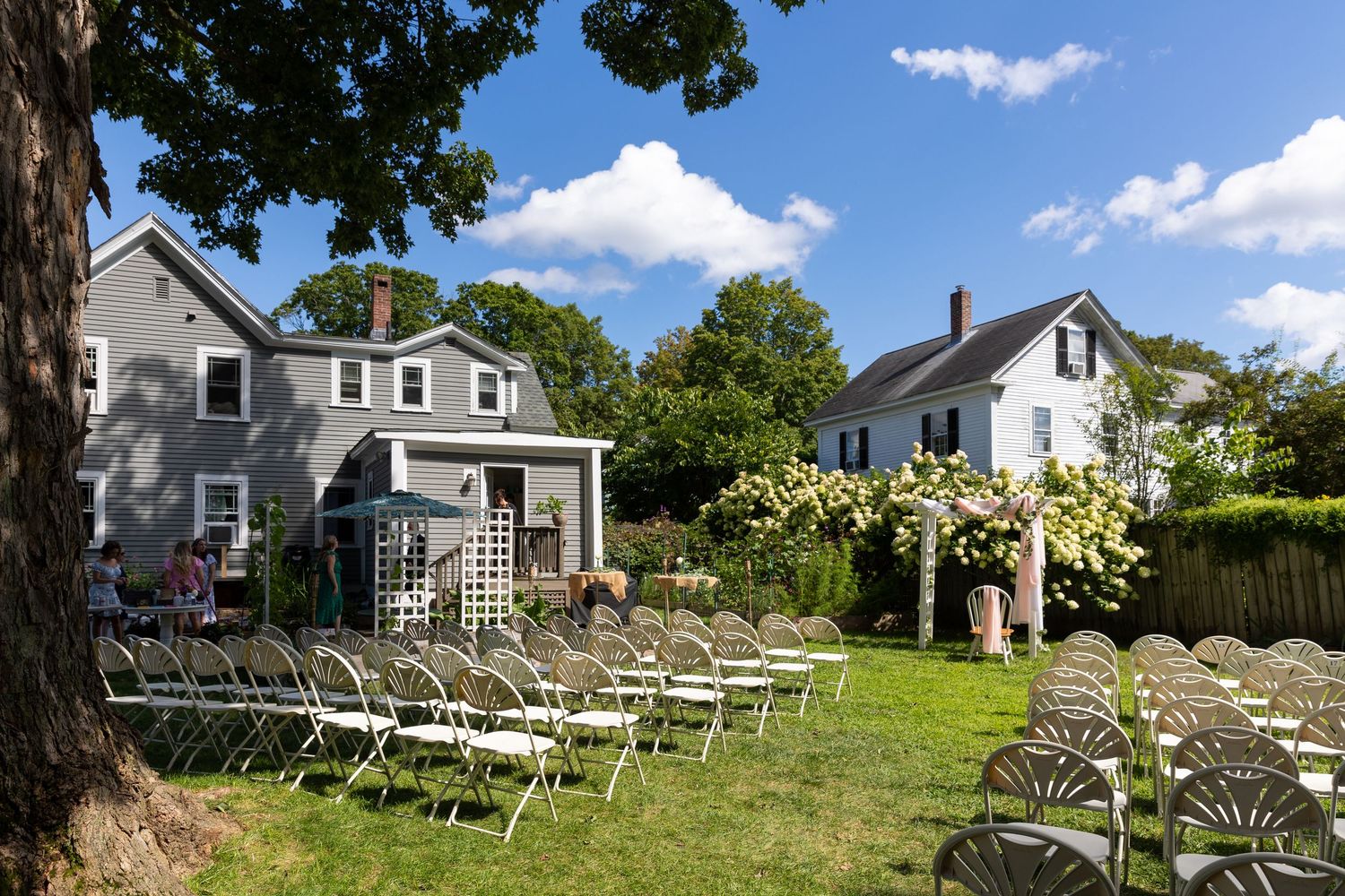 White farmhouse with rows of decorative dining chairs arranged on a hillside lawn creating a unique outdoor theater setup.