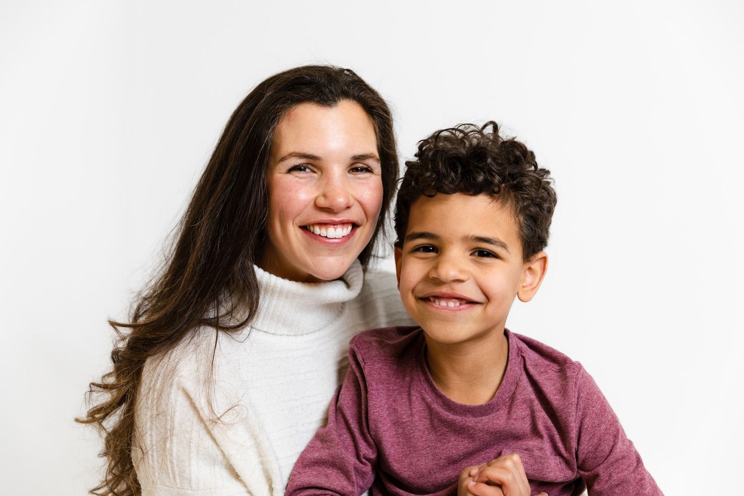 Two people in white sweaters share a warm moment together against white background.