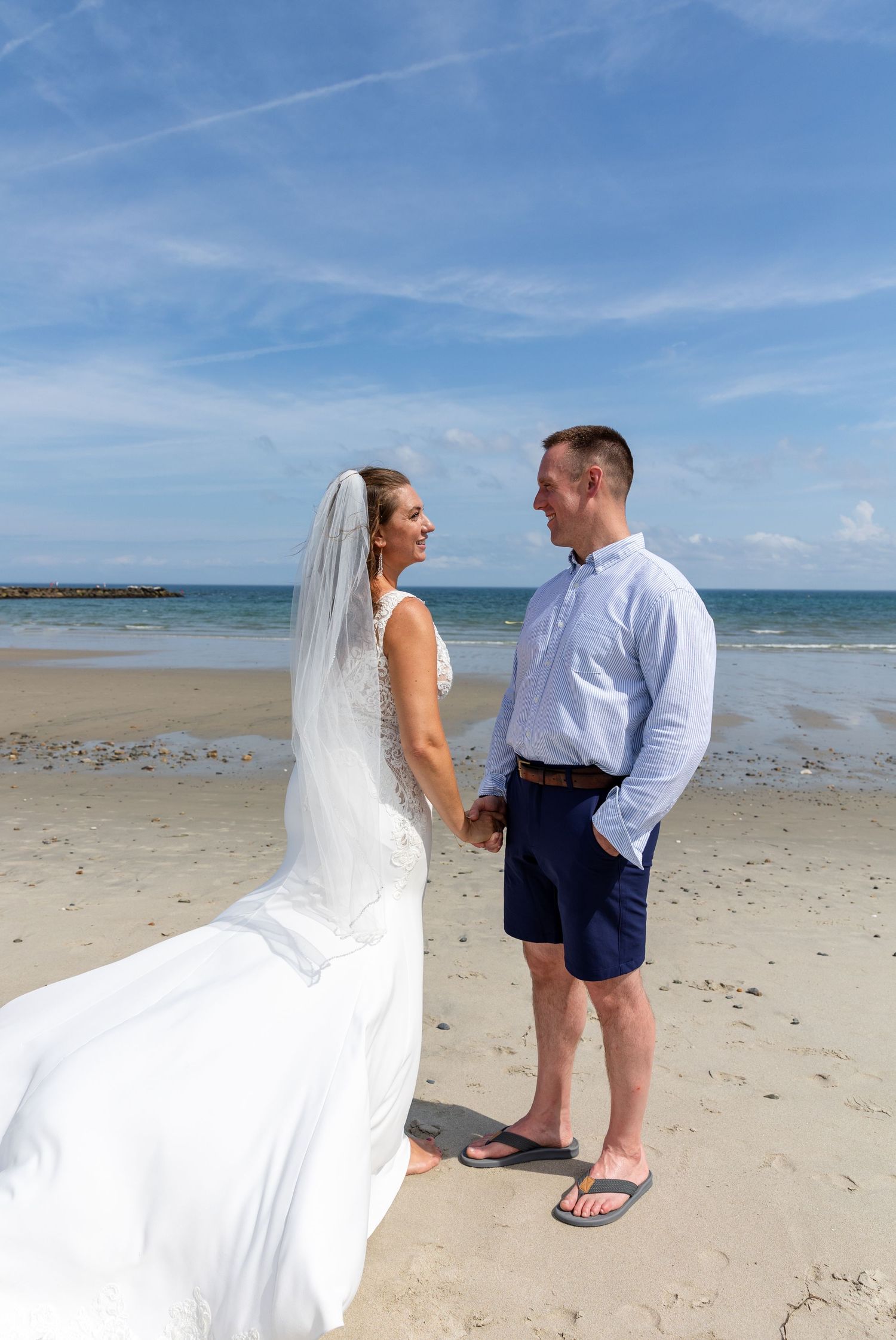 A couple shares a romantic moment together on a scenic beach with blue skies and ocean in the background.