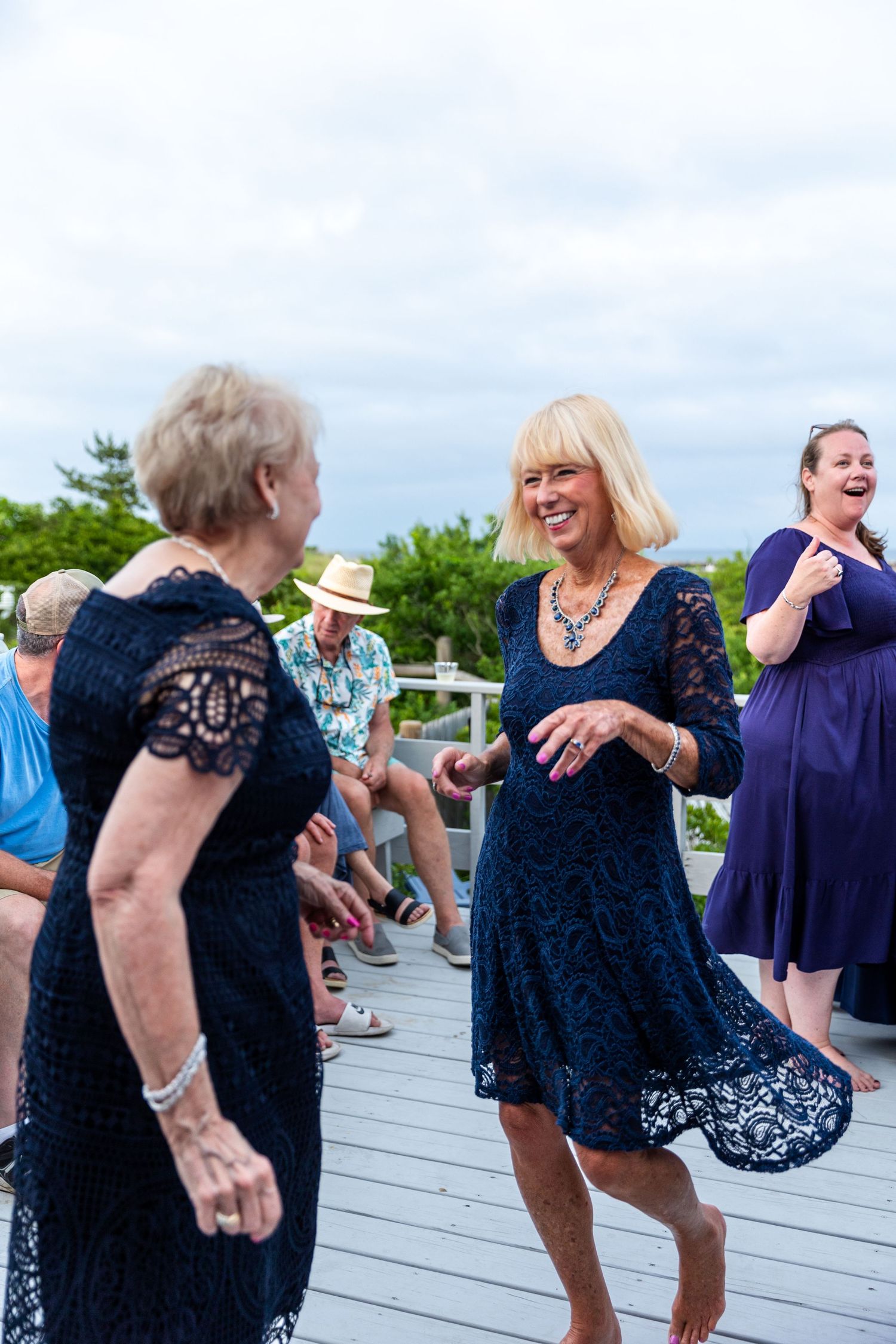 People dance and celebrate together on an outdoor wooden deck during a festive summer gathering.