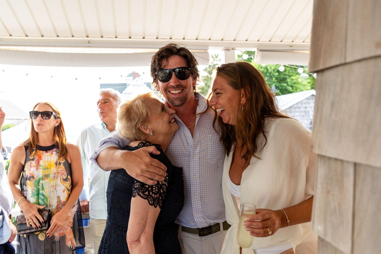 Joyful guests mingle and embrace at an outdoor wedding celebration under an elegant white columned venue.