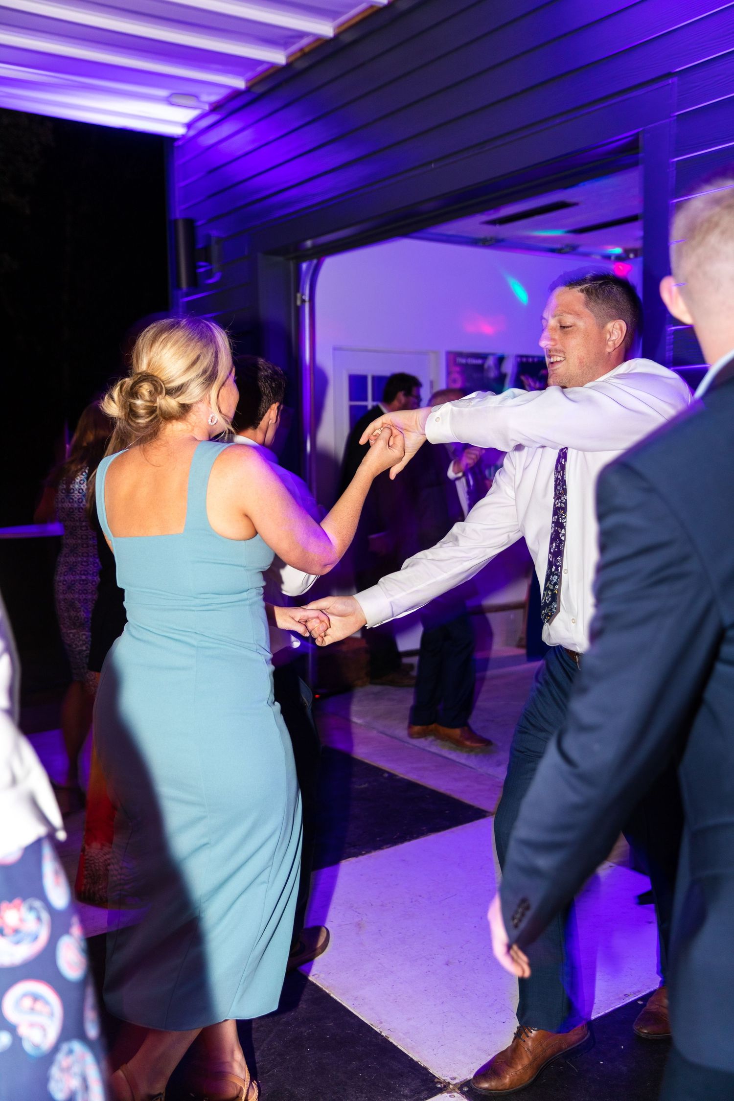 People dancing together at a party with purple lighting in the background at what appears to be an indoor venue.