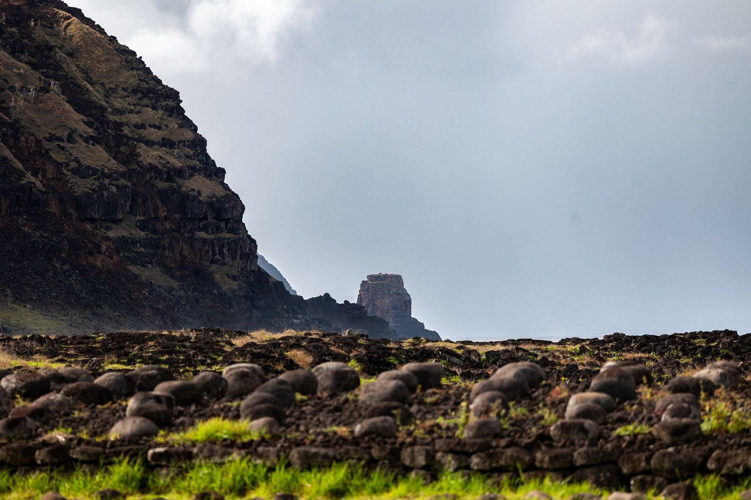 Dramatic panoramic view of dark volcanic cliffs along a rugged coastline under moody cloudy skies on Easter Island.