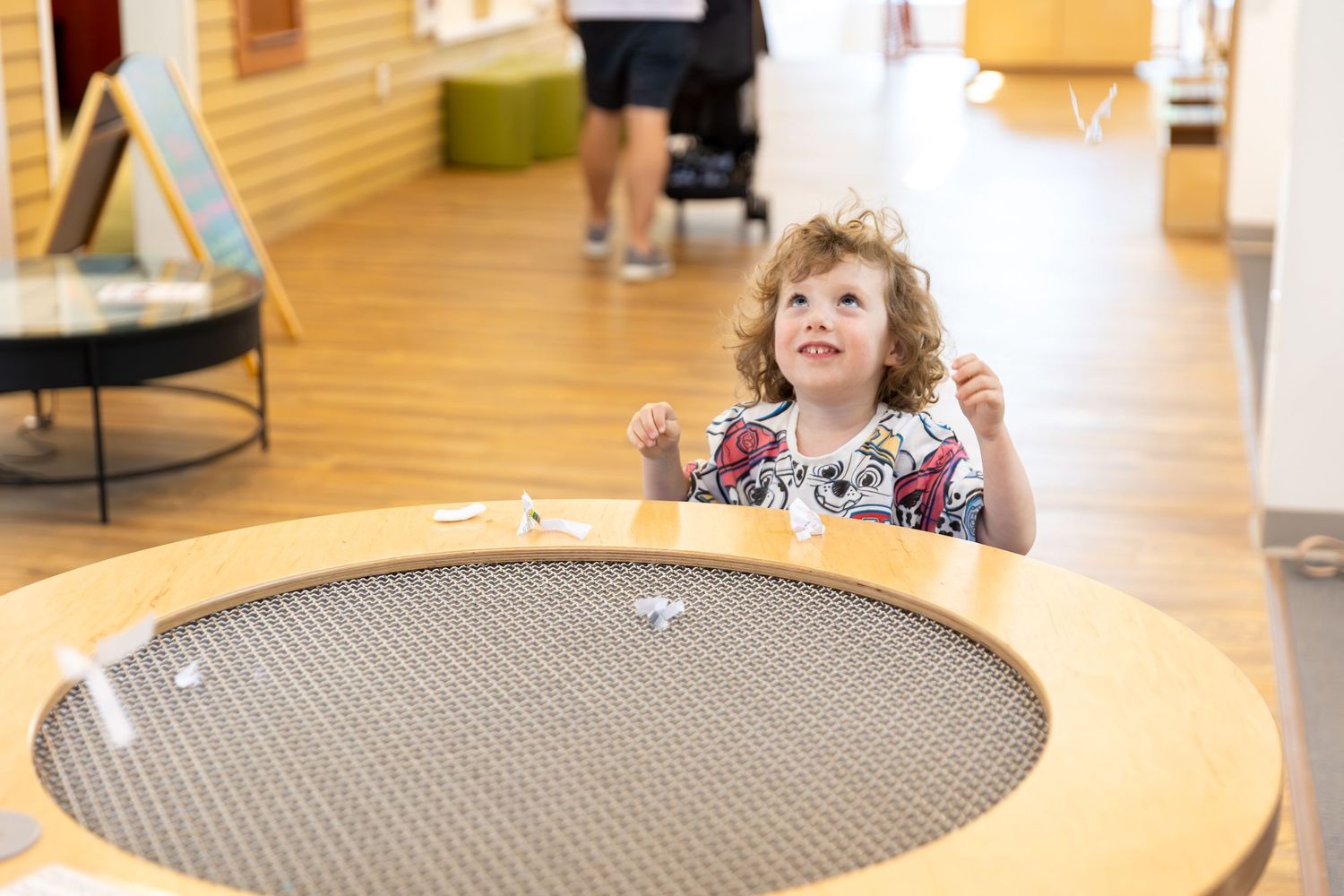 A person interacts with a large, circular metal mesh panel in a bright interior space.