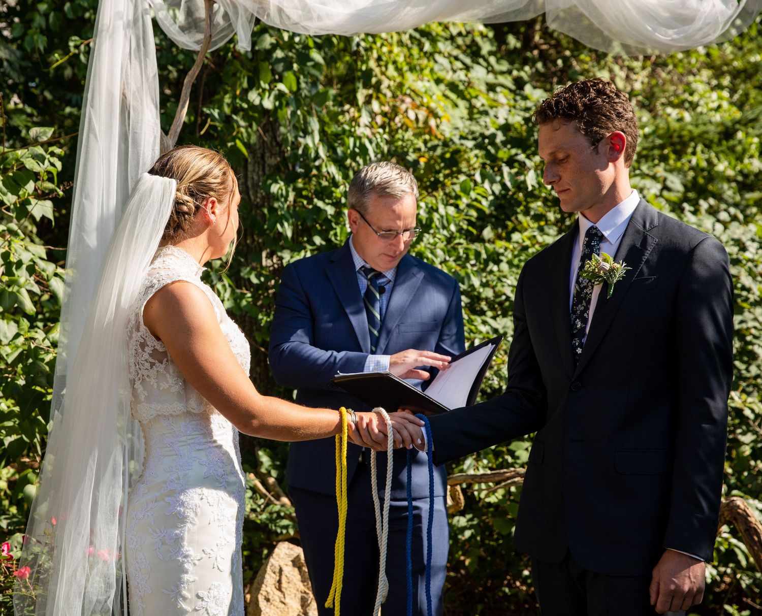 Outdoor ceremony scene with flowy white drapes and green foliage creating a beautiful garden wedding backdrop.