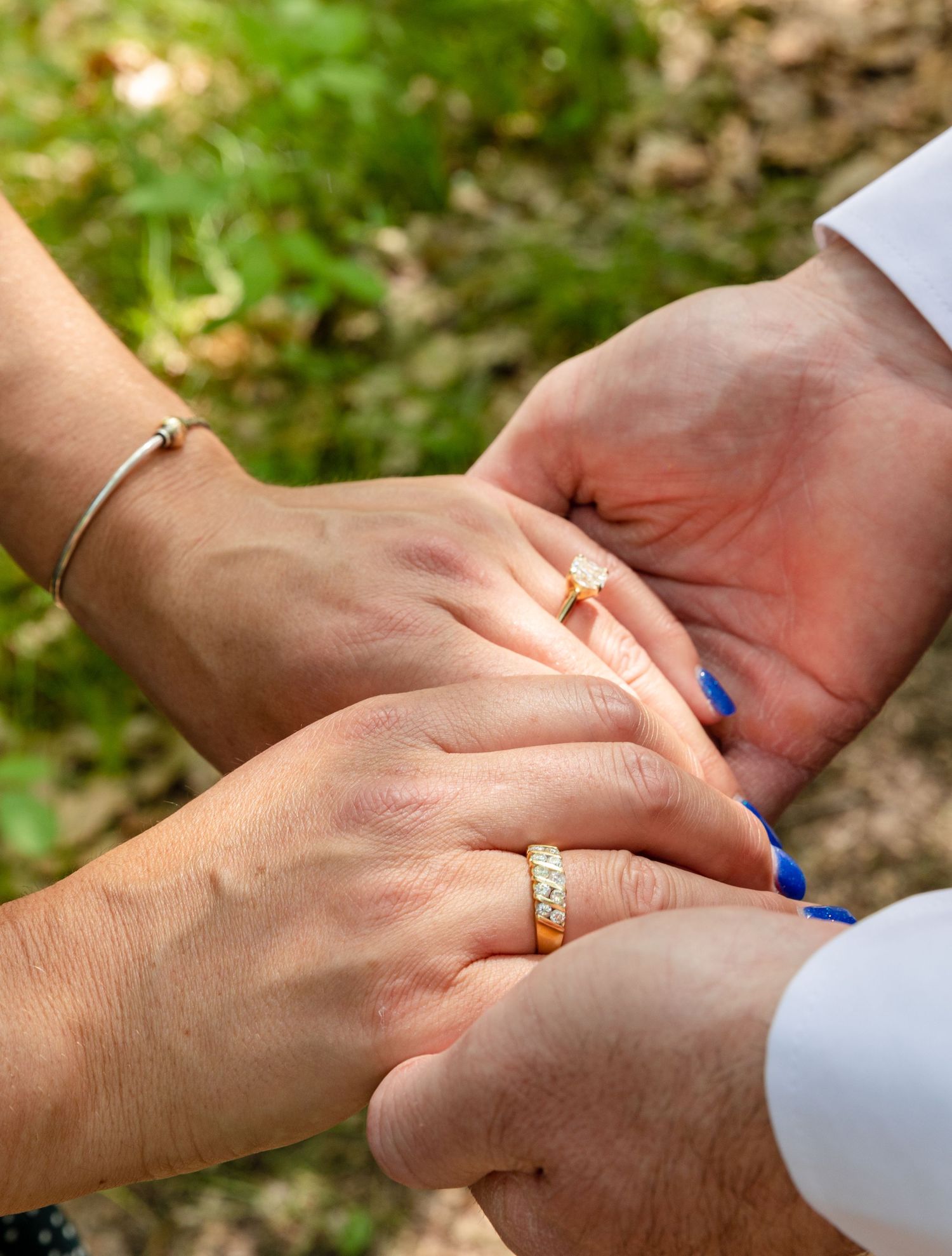 Close up shot of hands exchanging wedding rings during an outdoor ceremony with green foliage in the background.
