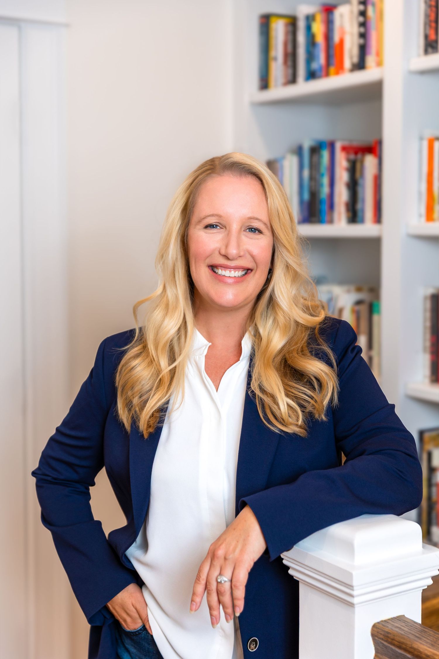 Professional business headshots in a navy blazer and white shirt shown against a bookshelf background in the office.