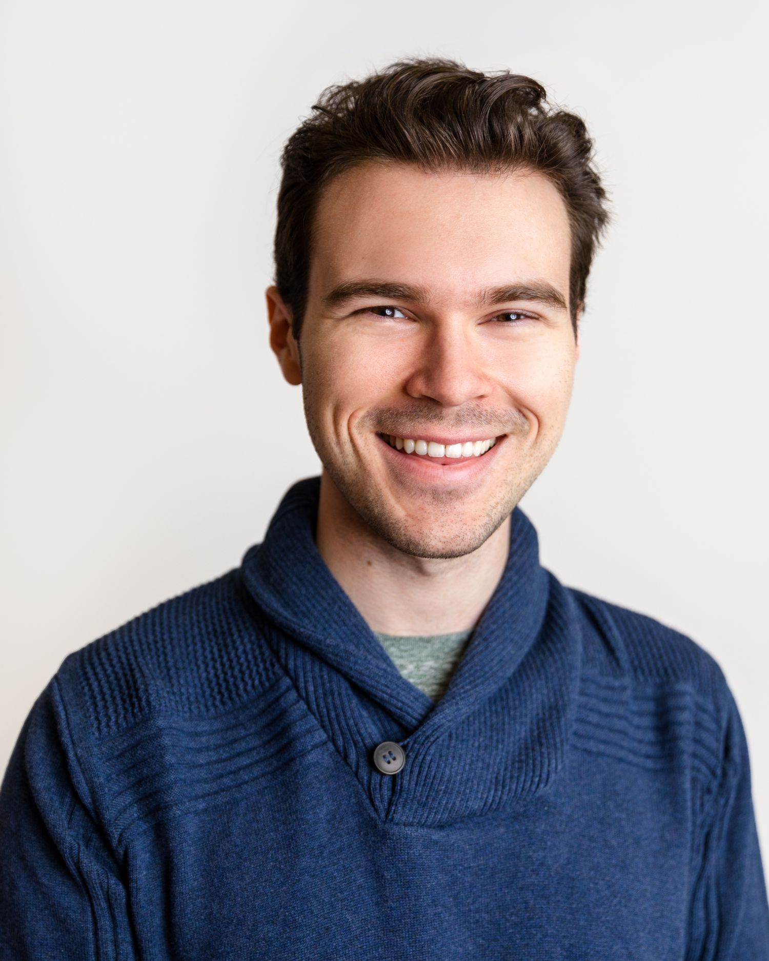 Professional headshot of person in navy sweater smiling against white background.