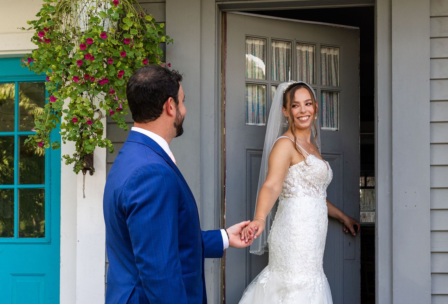 A bride and groom share a sweet moment at the entrance of a gray house with a bright turquoise door.