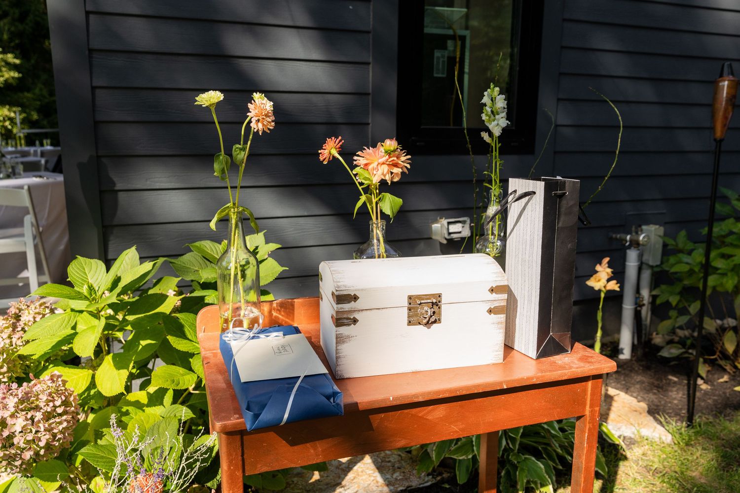 Rustic back porch decorated with wooden shelves displaying colorful flower pots and trailing vines against a dark wall.