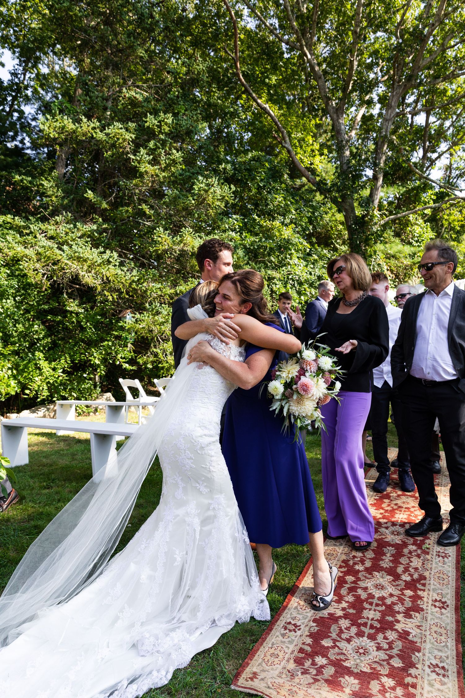 Wedding celebration on an outdoor patio with a beautiful ornate rug and table setting under lush green trees.