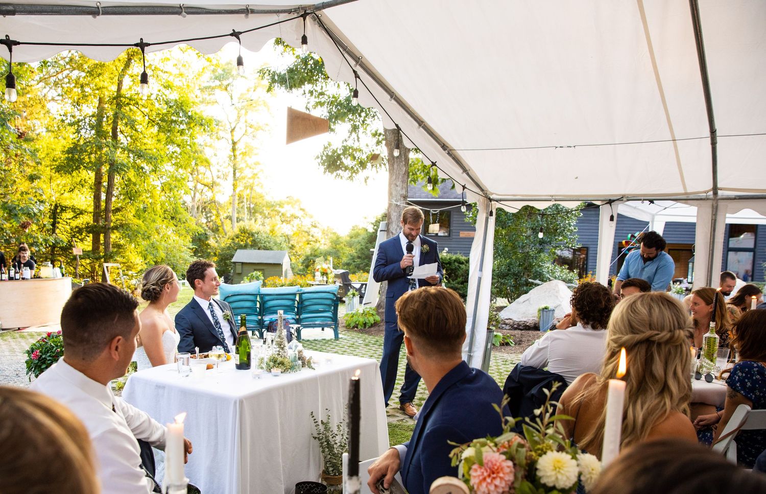 Wedding guests celebrate under a white outdoor tent during an elegant daytime reception.