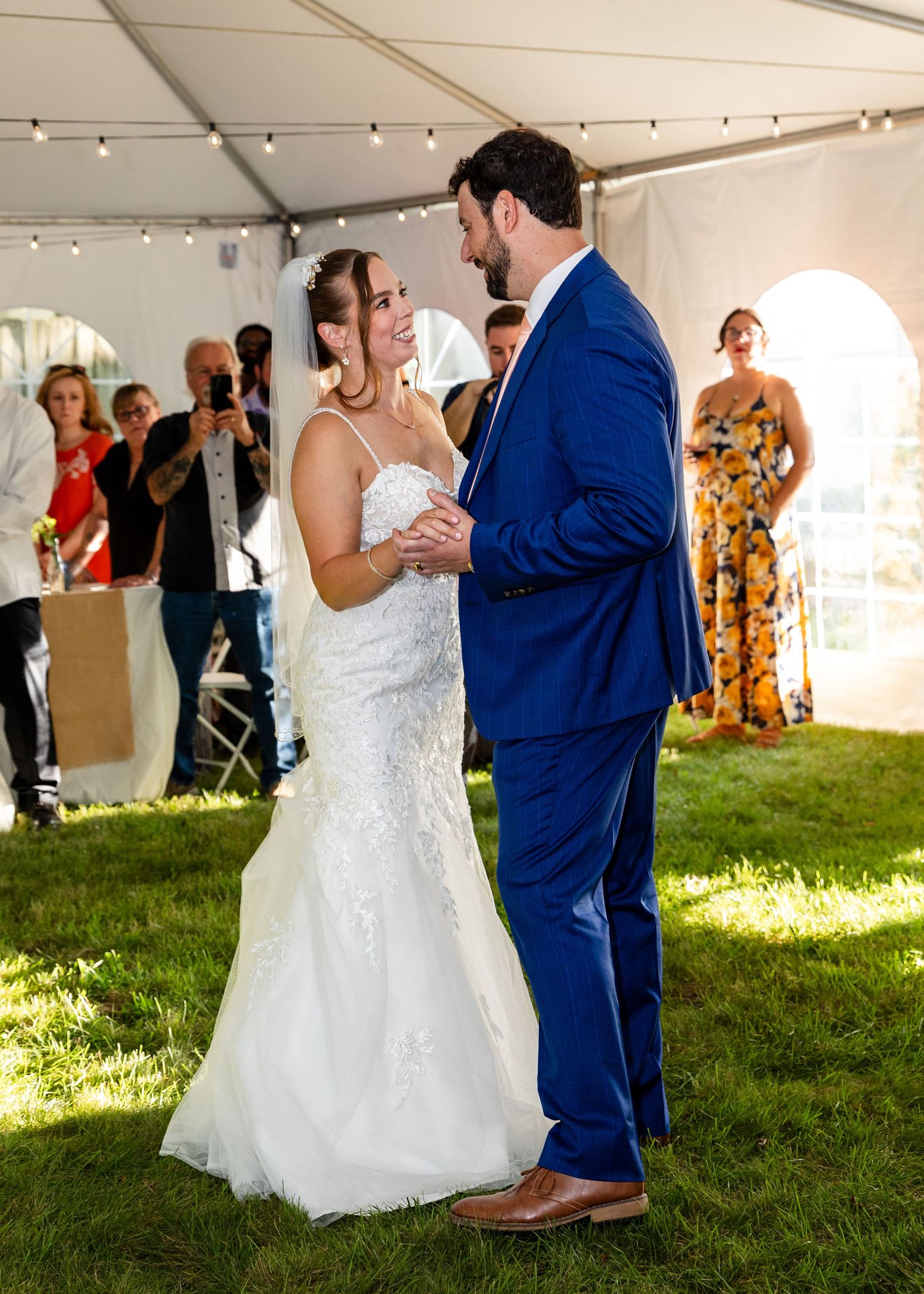 Bride and groom perform their coordinated first dance together under a white tent on a grassy lawn at sunset.