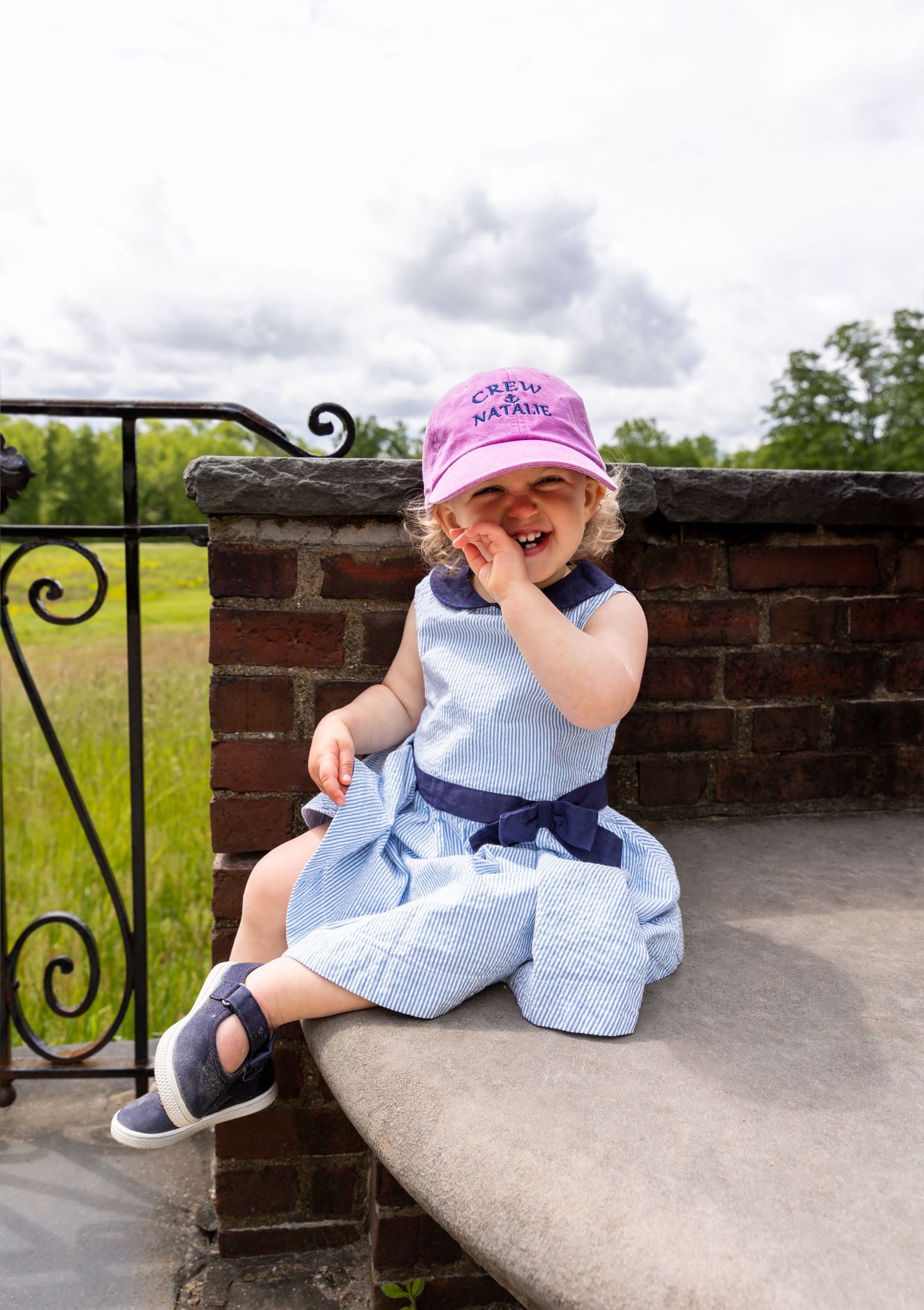 A small child in light blue clothes and pink hat plays on a brick wall structure on a cloudy day.