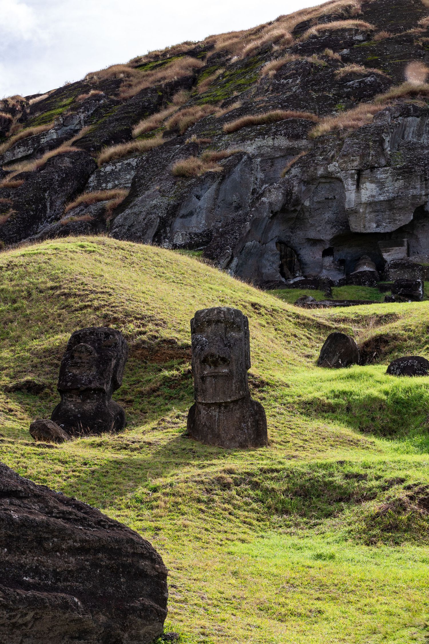 Ancient moai statues stand against grassy slopes and dark volcanic cliffs on Easter Island.
