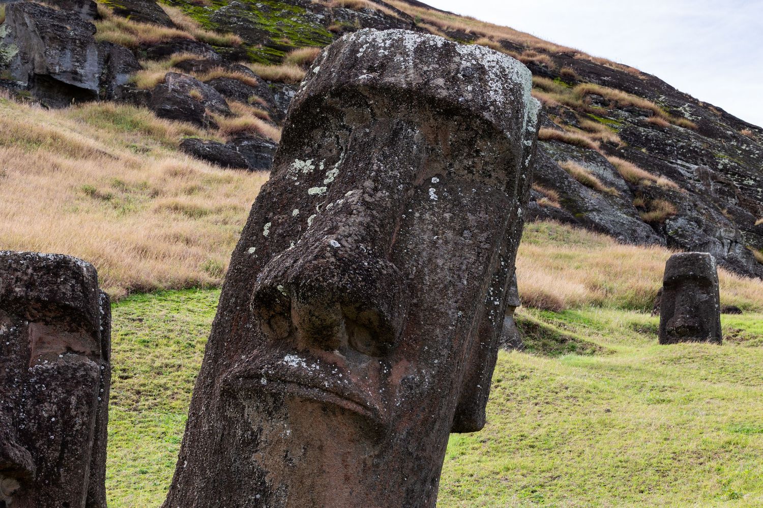 Ancient carved Moai statues stand silently along the rocky slopes of Easter Island at sunset.