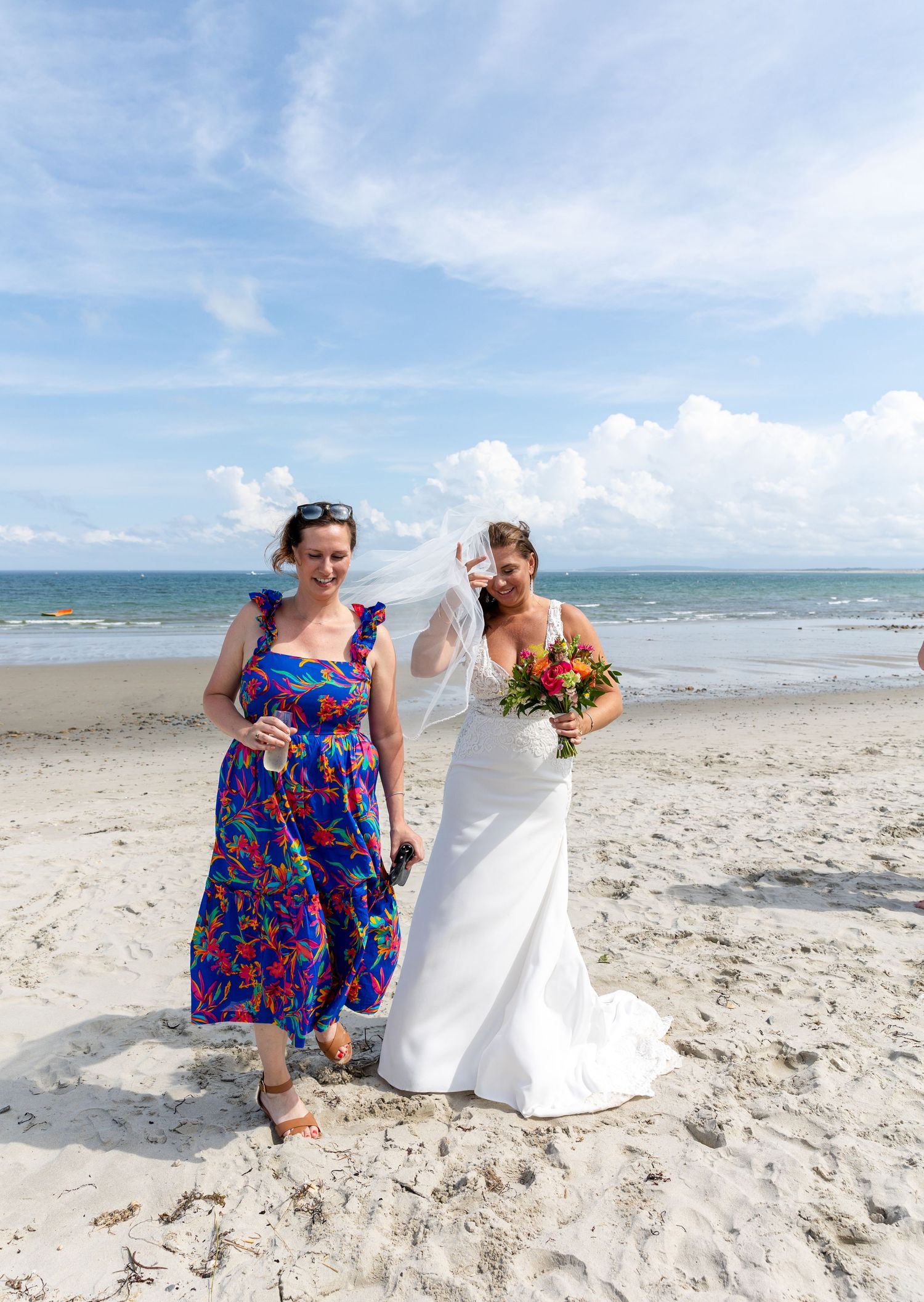 Two people share a joyful moment together while walking on a sunny white sand beach with ocean waves in the background.