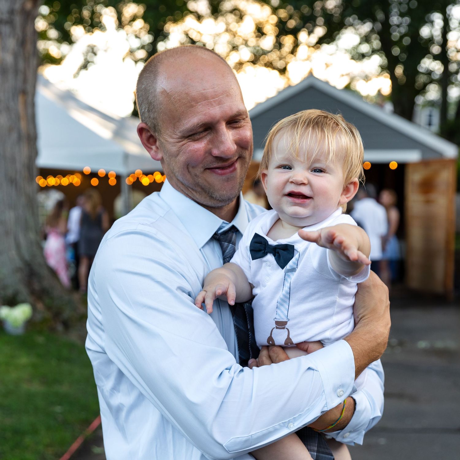 A joyful moment between a baby in white and an adult in light colored clothing outdoors.